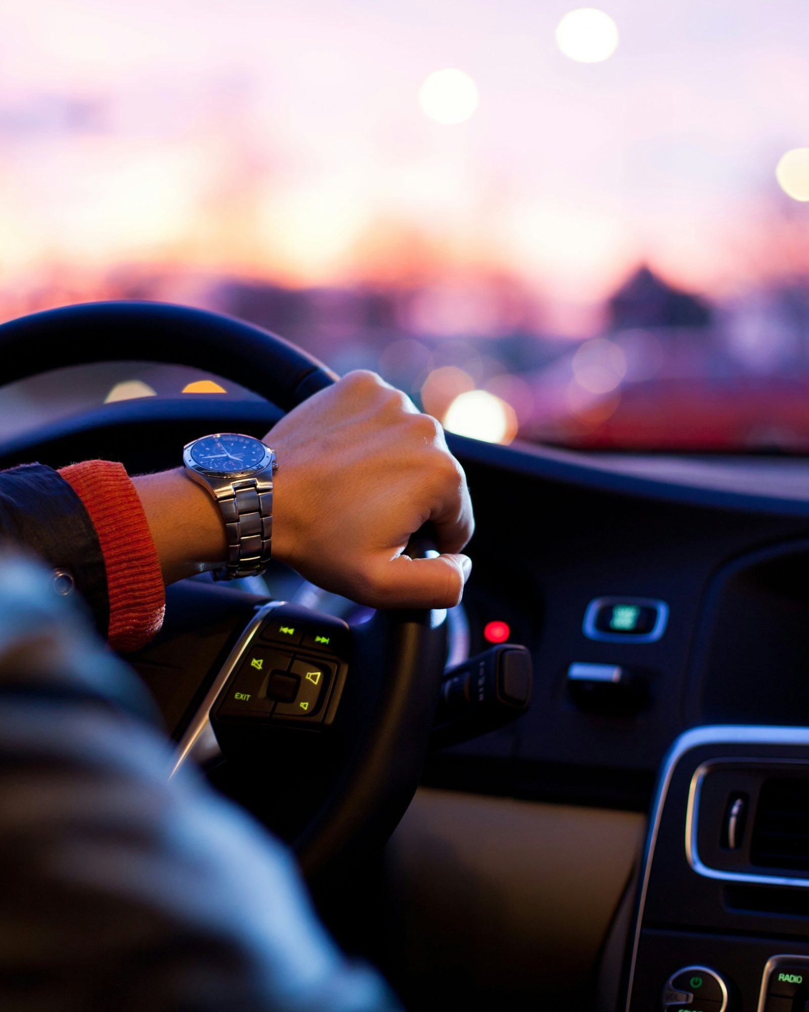 A driver’s hand resting on the wheel of a chauffeured car at dusk